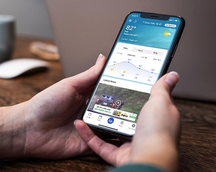A person holding their mobile phone looking at the weather app
